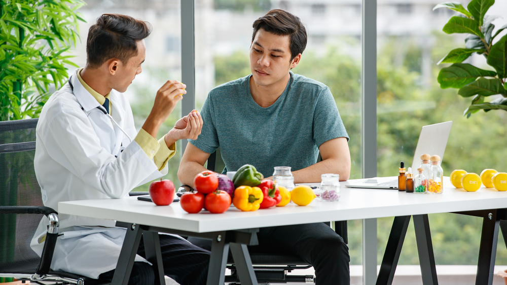 Male,Nutritionist,Showing,And,Discussing,Vitamin,Pills,With,Asian,Man